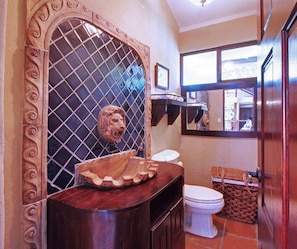 Un baño con tocador, inodoro, espejo y una escultura decorativa de cabeza de león.