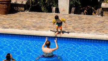 A swimming pool with a stone deck, a child in a yellow swimsuit, and a woman in a black swimsuit.