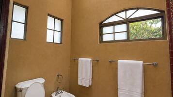 A bathroom with a toilet, bidet, and sink, two towels on towel racks, and a window with a view of trees.