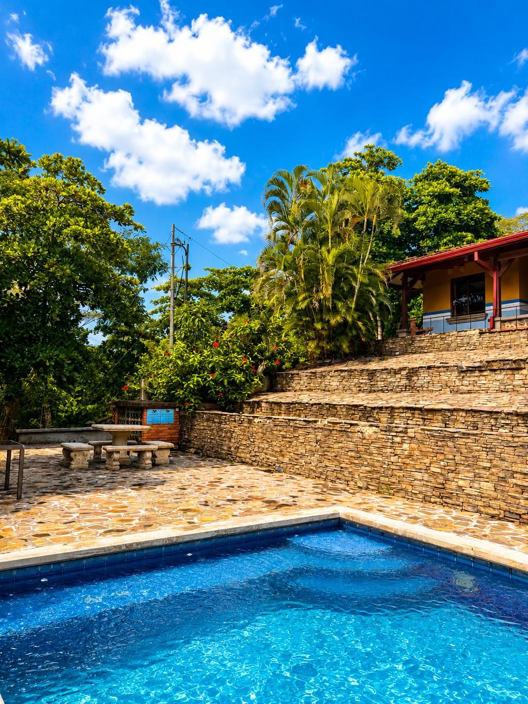 A swimming pool with stone tiles, a stone wall, and a bench.