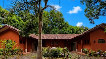 A two-story building with a red-tiled roof, surrounded by lush greenery and a clear blue sky.