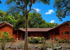 A two-story building with a red-tiled roof, surrounded by lush greenery and a clear blue sky.