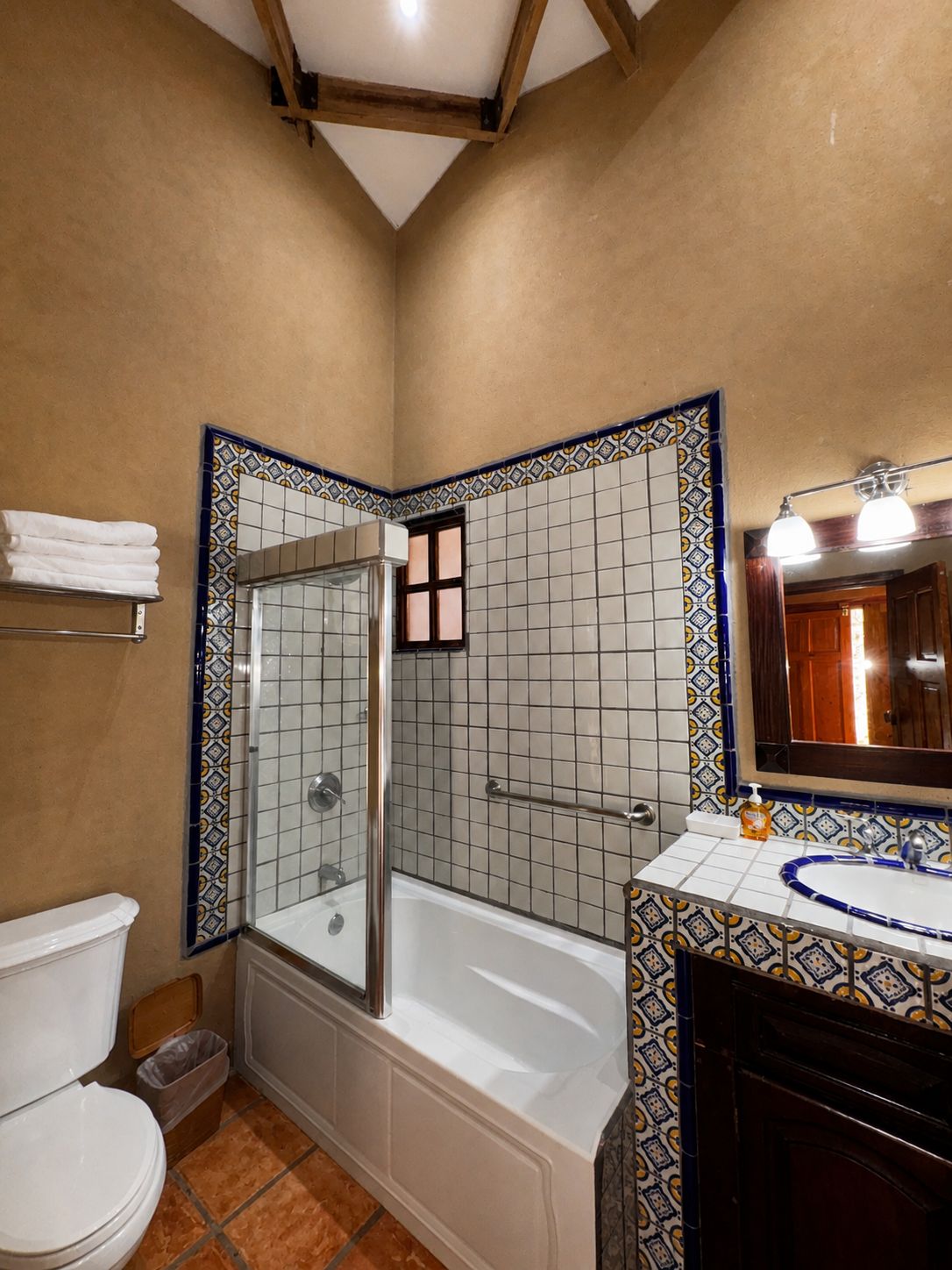A bathroom with a shower, toilet, and sink, featuring patterned tiles and wooden beams.