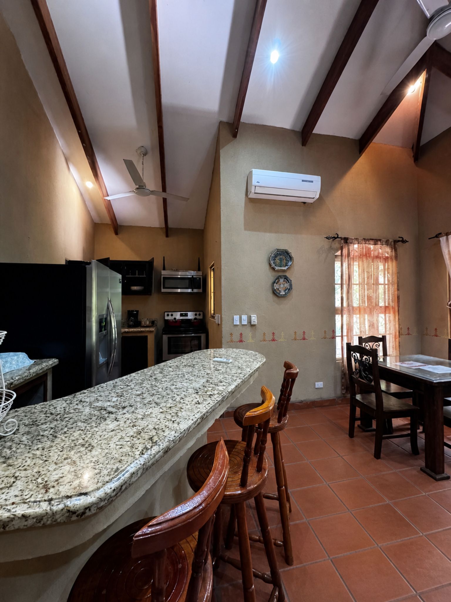 A kitchen with granite countertops, wooden chairs, a dining table, an air conditioner, and a ceiling fan.