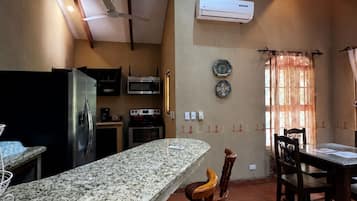 A kitchen with granite countertops, wooden chairs, a dining table, an air conditioner, and a ceiling fan.