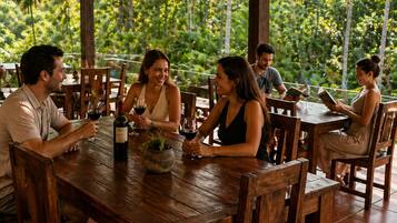 Un comedor al aire libre con mesas y sillas de madera, rodeado de abundante vegetación.