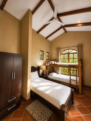 A bedroom with a large wardrobe, a single bed, two bunk beds, a ceiling fan, and a window with curtains.