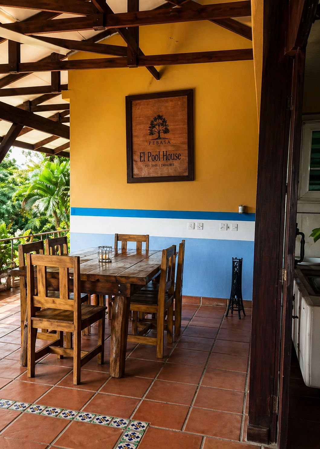 A wooden table with chairs under a wooden beam structure, a framed sign on the wall, and a tiled floor.