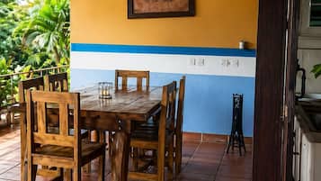 A wooden table with chairs under a wooden beam structure, a framed sign on the wall, and a tiled floor.