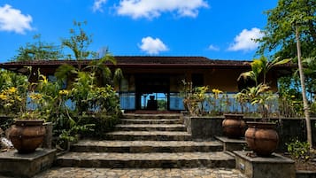 A building with a tiled roof, a staircase leading to a covered entrance, and potted plants around the steps.
