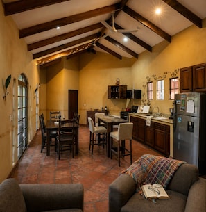 A spacious kitchen with wooden beams, a dining area with chairs, a sofa with a blanket, and a refrigerator. - Ocho Villas (Coyolar)