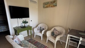 A living room with wicker furniture, a flat-screen TV, a green console table, and a painting on the wall. - Amazing ocean views (Castries)