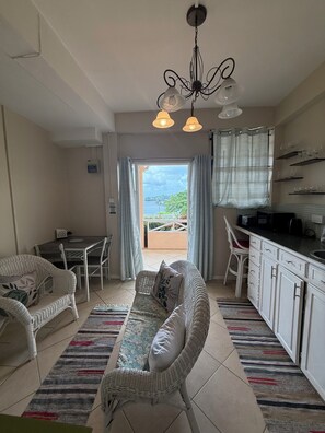 A living room with a sofa, chairs, a dining table, and a kitchen area with cabinets and a microwave. - Belle Escape- Green Room (Castries)