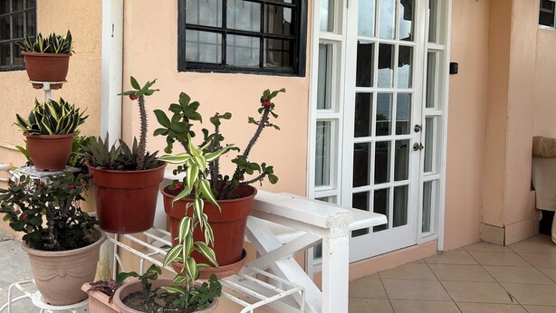 A balcony with potted plants, a white table, and a window with a black frame. - Amazing ocean views (Castries)