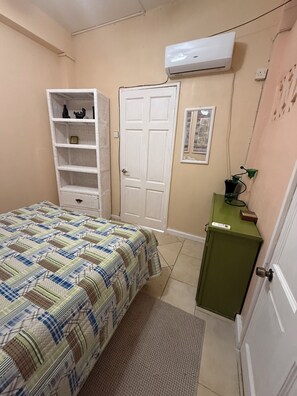 A bedroom with a bed, a wardrobe, a small cabinet, an air conditioning unit, and a door. - Belle Escape- Green Room (Castries)