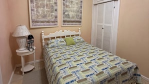 A bedroom with a bed, a ceiling fan, two wall-mounted pictures, a bedside table with a lamp, and a door with louvered shutters. - Amazing ocean views (Castries)