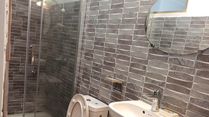 Une salle de bain avec une douche à parois de verre, des toilettes, un lavabo et une poubelle.