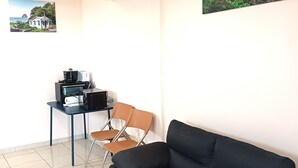 Une pièce avec un canapé noir, une petite table sur laquelle se trouve une machine à café, deux chaises et deux tableaux encadrés accrochés aux murs.