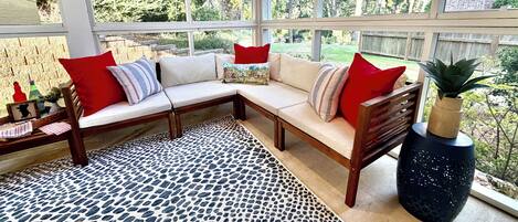 A sunlit room with a sectional sofa, a woven rug, and a potted plant.