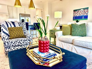 A living room with a sofa, a chair, a coffee table with books and a decorative item, a lamp, and a painting on the wall. - "Ole Rebel" - by OVR (Oxford)