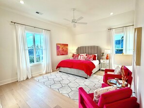Ein Schlafzimmer mit Bett, Stuhl, Nachttisch, Fenster und Deckenventilator.