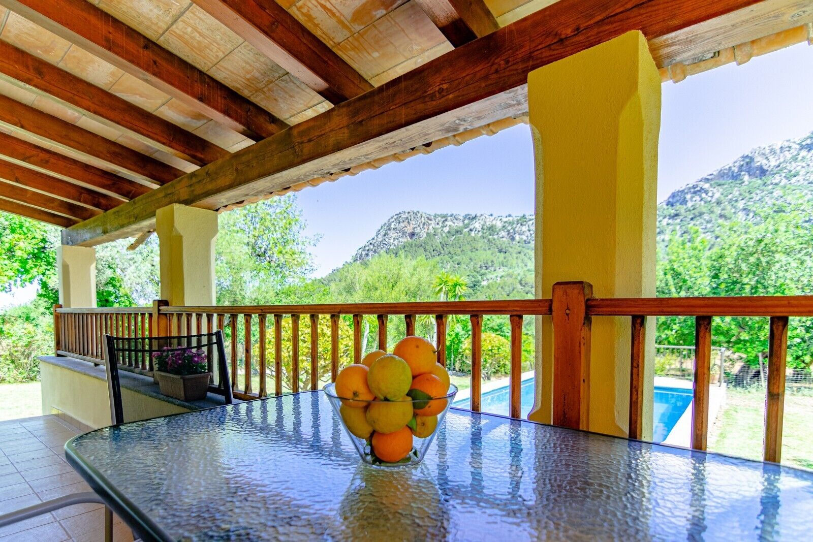 A covered outdoor area with a glass table, a chair, and a fruit bowl.