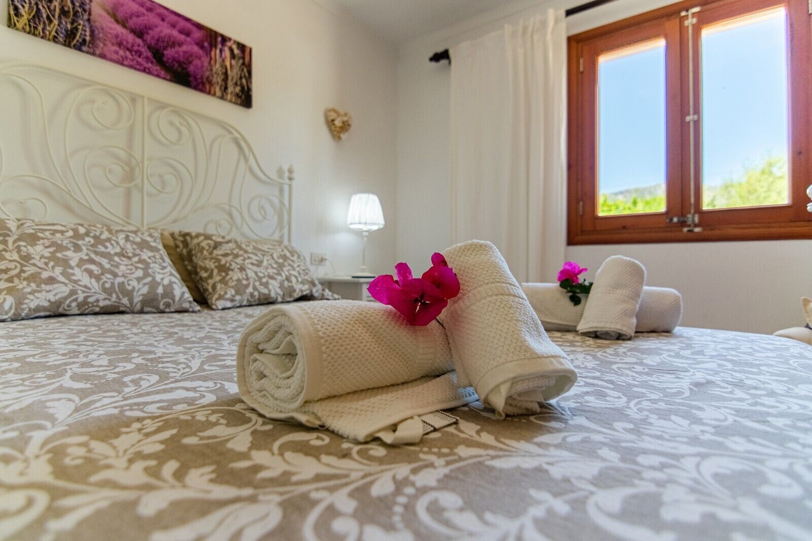 A hotel room with a bed, pillows, a nightstand, a lamp, and a window with curtains.