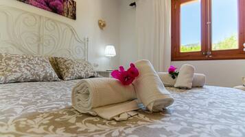 A hotel room with a bed, pillows, a nightstand, a lamp, and a window with curtains.