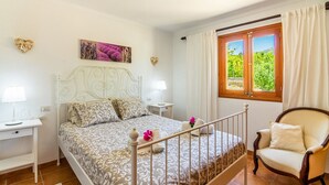 A bedroom with a bed, bedside tables, a chair, a window with curtains, and a painting on the wall. - Can Pep – Country House in Pollensa with Pool (Pollenca)