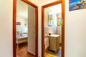 A hallway leading to a bedroom with a bed and a bathroom with a sink and mirror. - Can Pep – Country House in Pollensa with Pool (Pollenca)