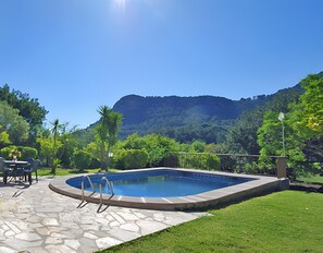 Una piscina con patio de piedra, rodeada de vegetación y un paisaje montañoso.