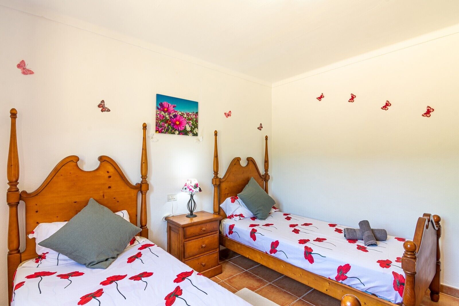 Un dormitorio con dos camas de madera, cada una con una colcha y almohadas estampadas. Hay una mesita de noche con una lámpara entre las camas.