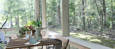 A wooden table with a bottle and glasses, a plant, and a decorative item on a balcony with a view of a forest.