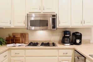 A kitchen with white cabinets, a stainless steel microwave, a gas stove, a coffee maker, and a cutting board. - "Hillside Hideaway" by OVR (Oxford)