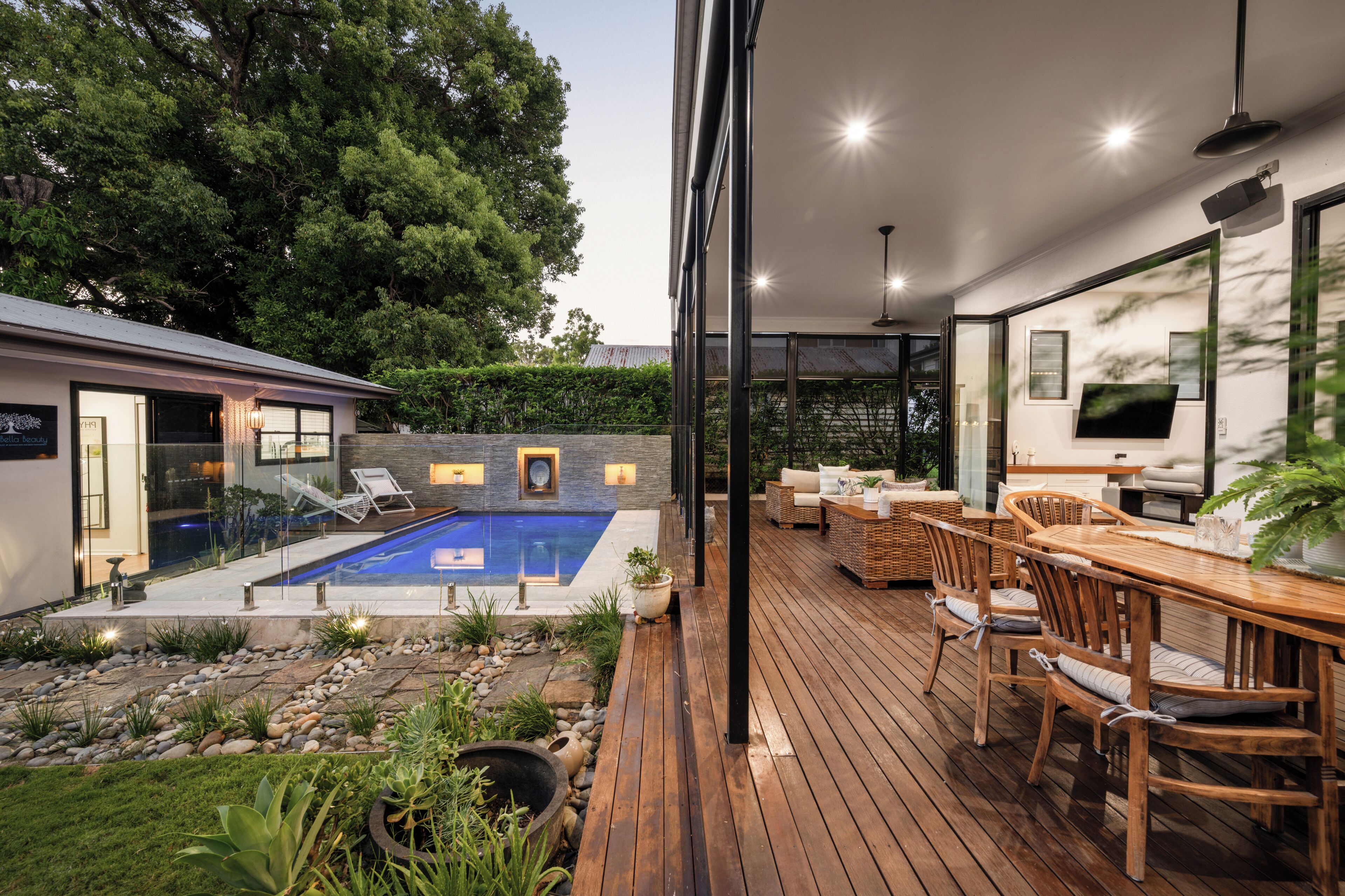 A modern outdoor patio with a wooden deck, a pool, and a seating area with wicker furniture.