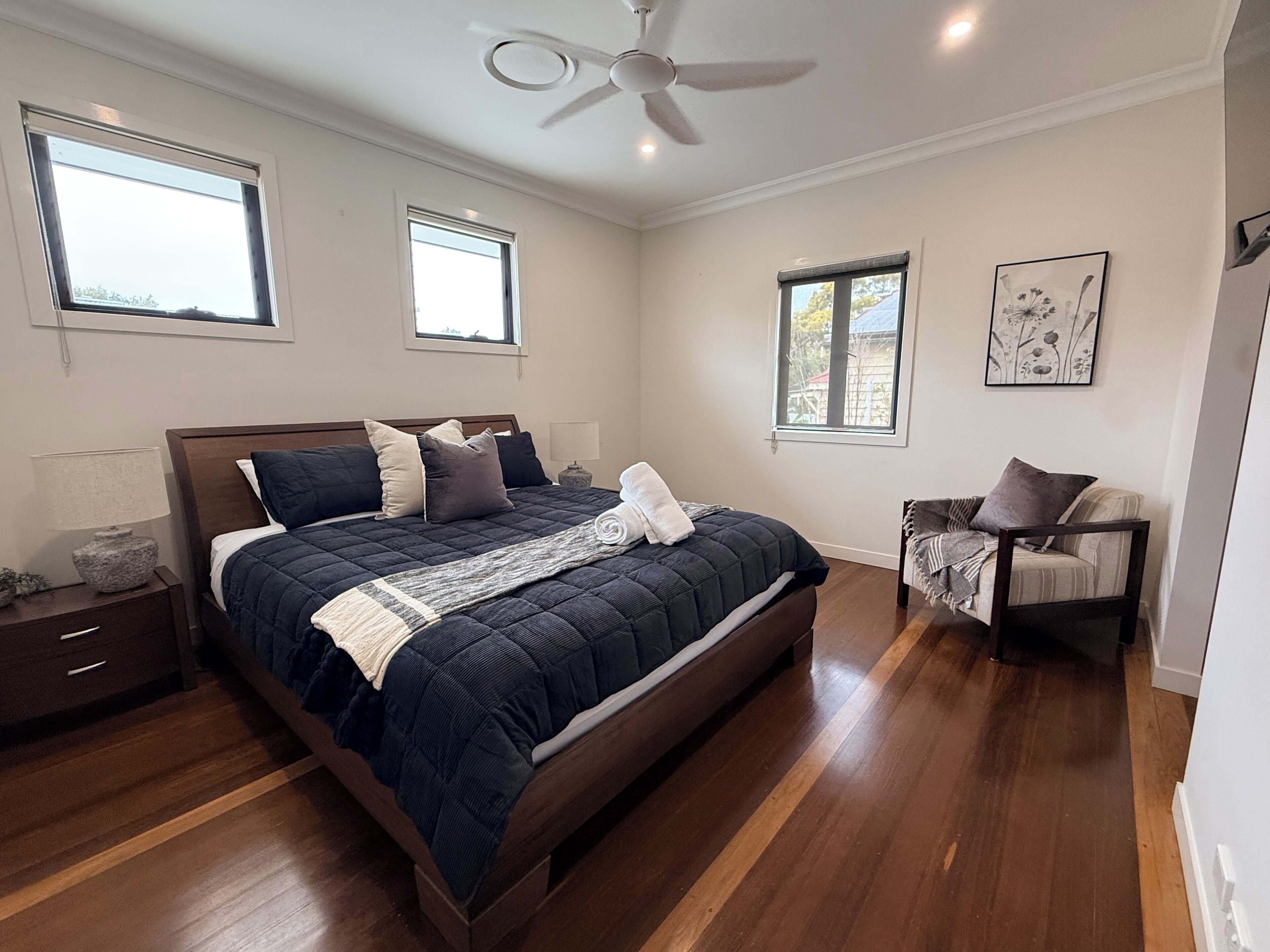 A bedroom with a large bed, two bedside tables, a ceiling fan, and two windows.