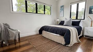 A bedroom with a large bed, two bedside tables, a chair, and a window.