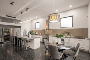 A modern kitchen with a central island, bar stools, and a dining table with chairs.