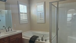 Un baño con tocador doble lavamanos, bañera e hidromasaje a nivel del suelo.