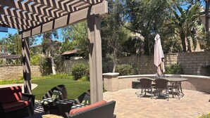 Un patio al aire libre con una pérgola, disposición de asientos y un muro de ladrillo.