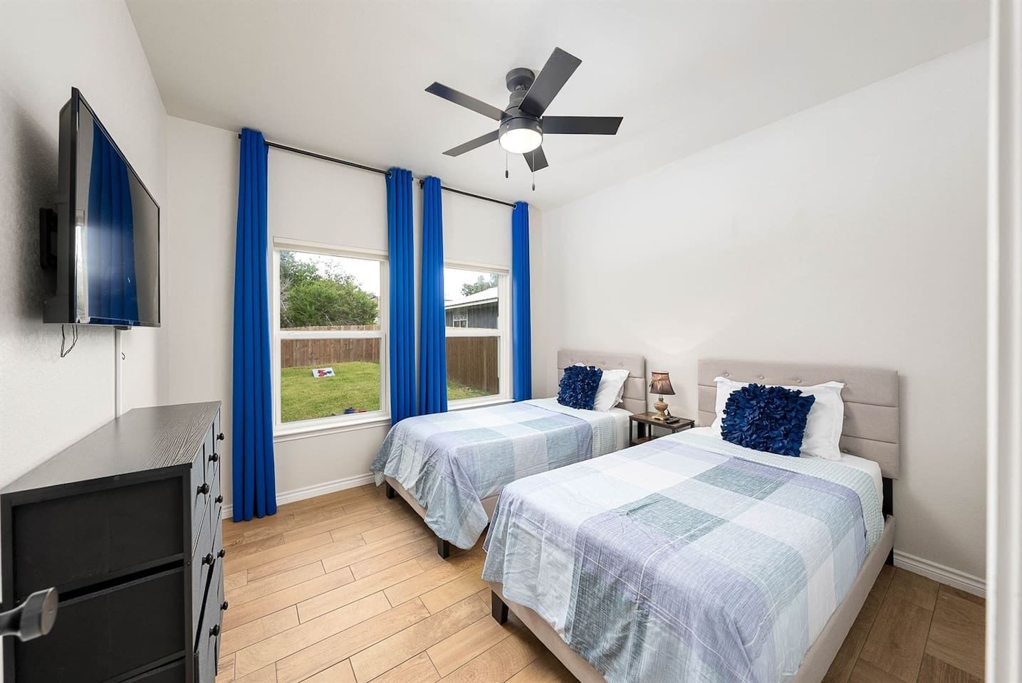A bedroom with two beds, a ceiling fan, a TV, and a view of the backyard.