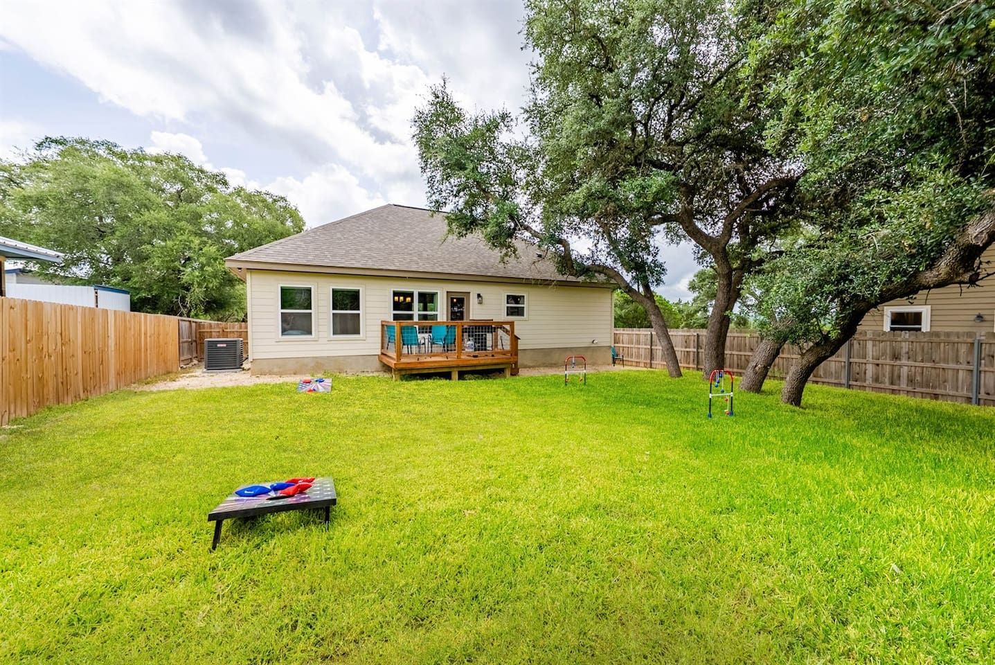 A residential backyard with a wooden deck, a trampoline, and a tree.