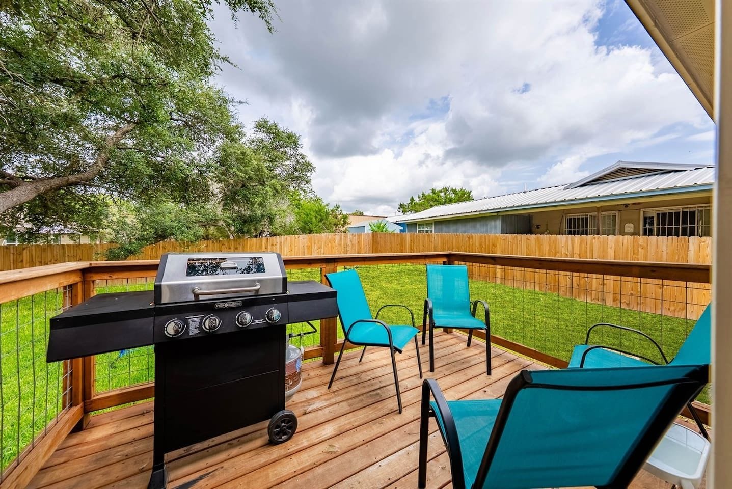An outdoor deck with a barbecue grill, two chairs, and a wooden fence.