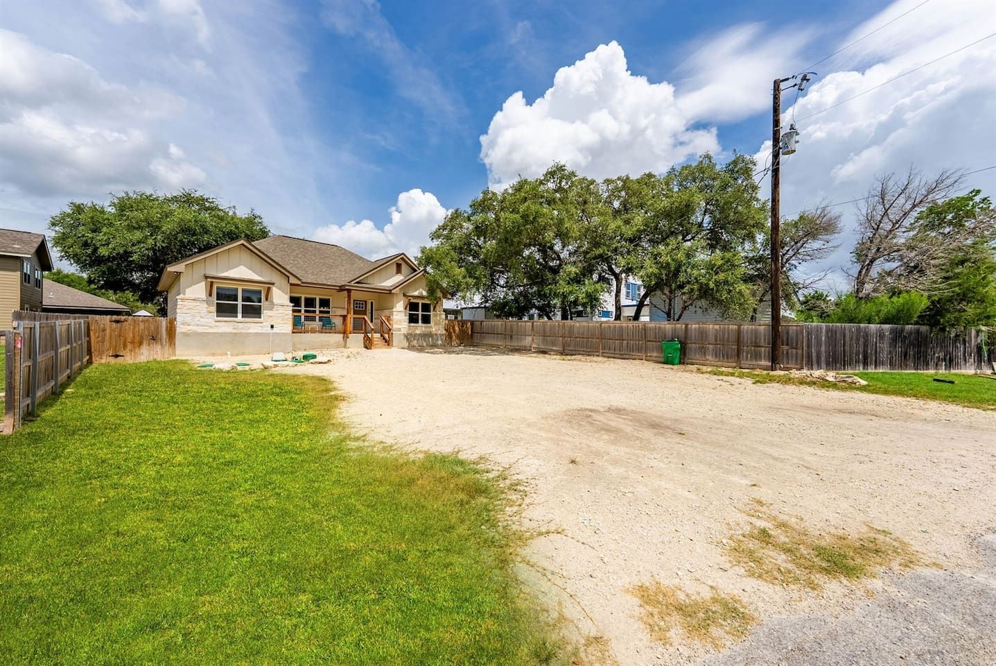 A residential property with a fenced backyard, a house with a stone facade, and a clear sky.