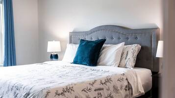 A neatly made bed with a floral bedspread, a grey upholstered headboard, and two bedside lamps.