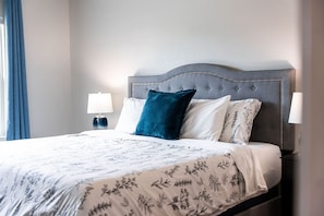 A neatly made bed with a floral bedspread, a grey upholstered headboard, and two bedside lamps. - Near Boat Ramp #6 | Boat Parking + Huge Yard (Canyon Lake)