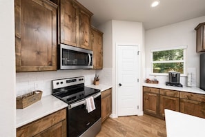 A kitchen with wooden cabinets, a stainless steel microwave, an oven, and a coffee maker on the counter. - Near Boat Ramp #6 | Boat Parking + Huge Yard (Canyon Lake)