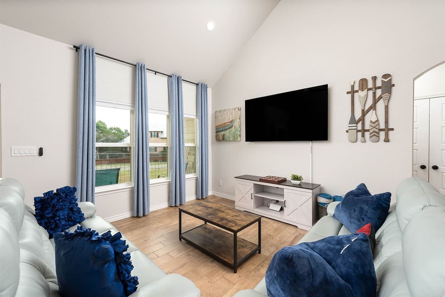 A modern living room with a flat-screen TV, a wooden coffee table, and a white sofa with blue cushions.