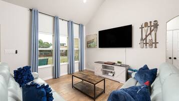 A modern living room with a flat-screen TV, a wooden coffee table, and a white sofa with blue cushions.