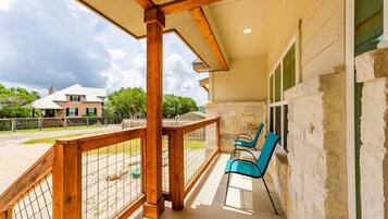 A covered outdoor area with a wooden railing, two chairs, and a view of a house in the background.